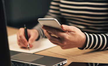 Woman writing contact list from mobile phone into her business agenda notebook for backup